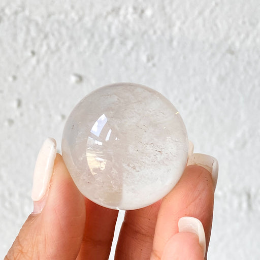 A person holding a clear quartz sphere healing crystal.